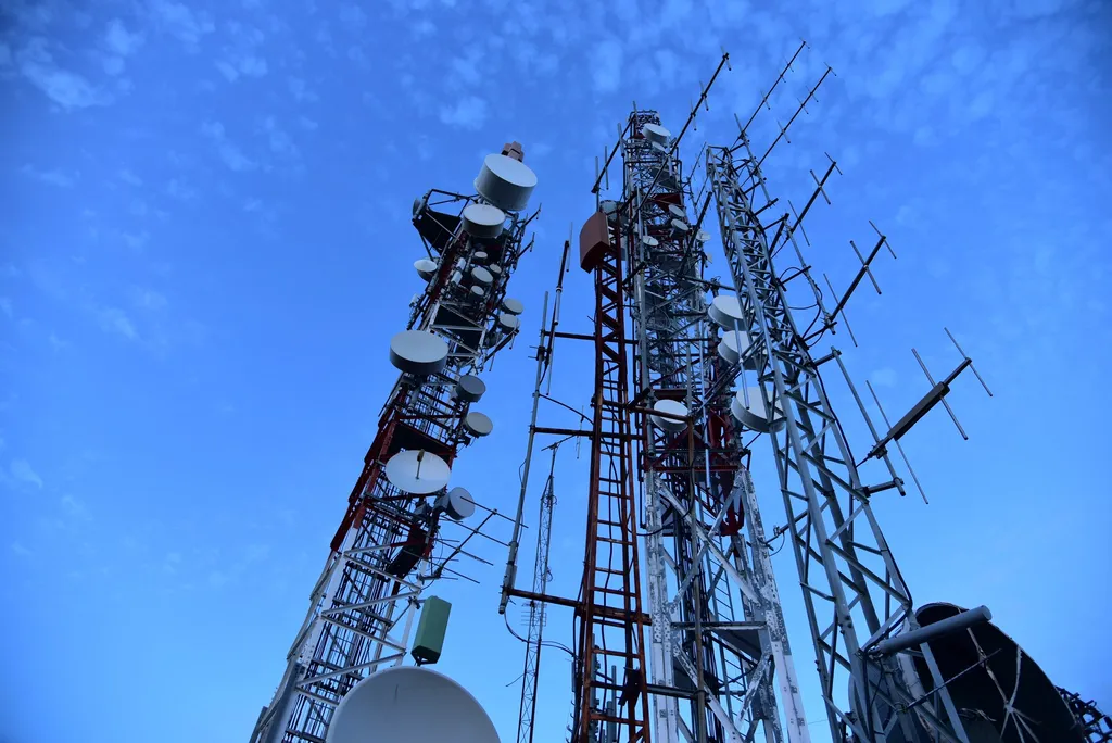 Telecom towers with microwave dishes and antennas against a blue sky